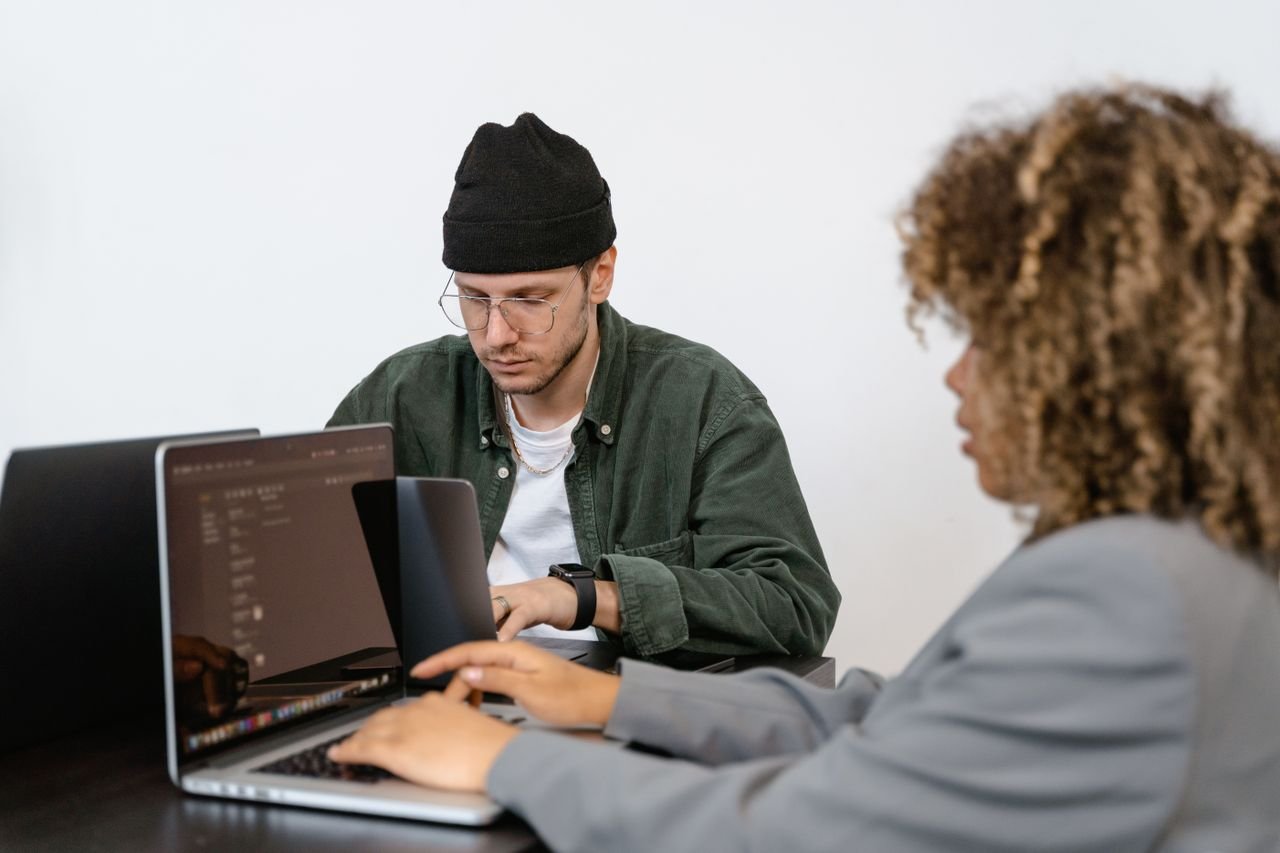 Two professionals working intently on laptops in a modern collaborative office environment.